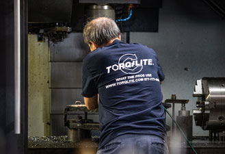 A worker in a TorqLite shirt uses industrial alignment tools.