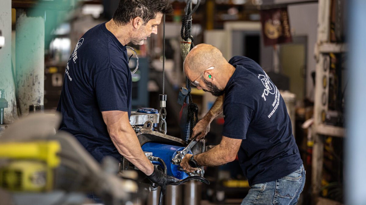 Two men operating a machine in a factory setting, focused on their tasks and collaborating on the equipment.