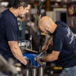 Two men operating a machine in a factory setting, focused on their tasks and collaborating on the equipment.