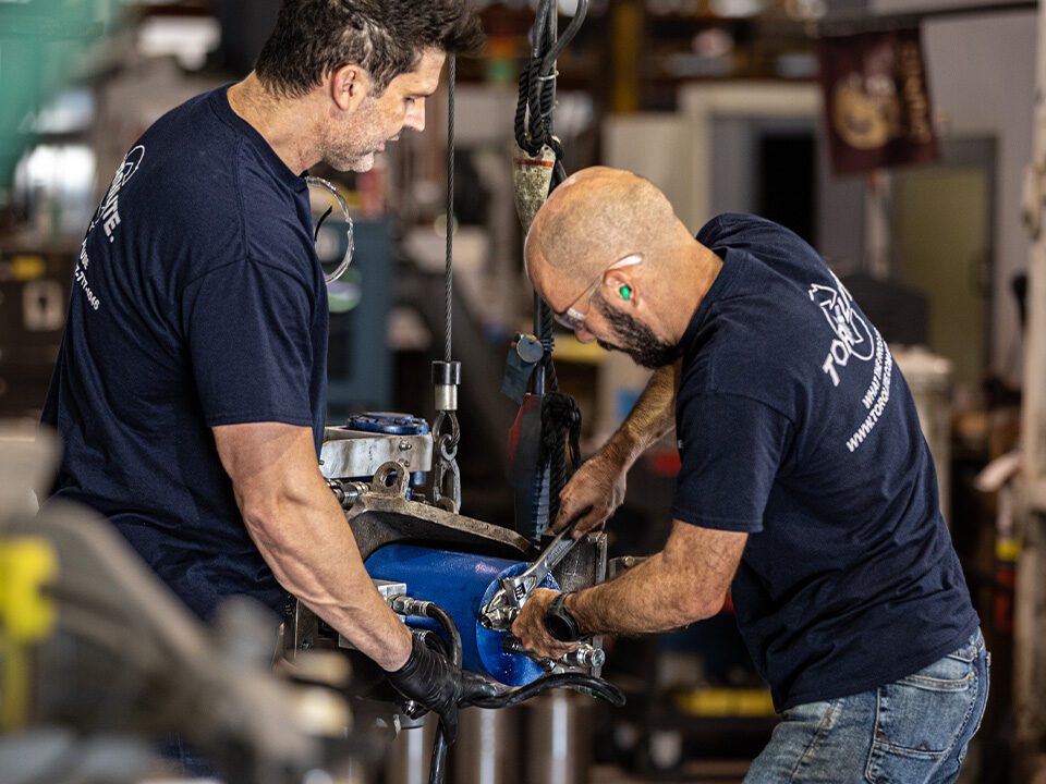 Two men operating a machine in a factory setting, focused on their tasks and collaborating on the equipment.